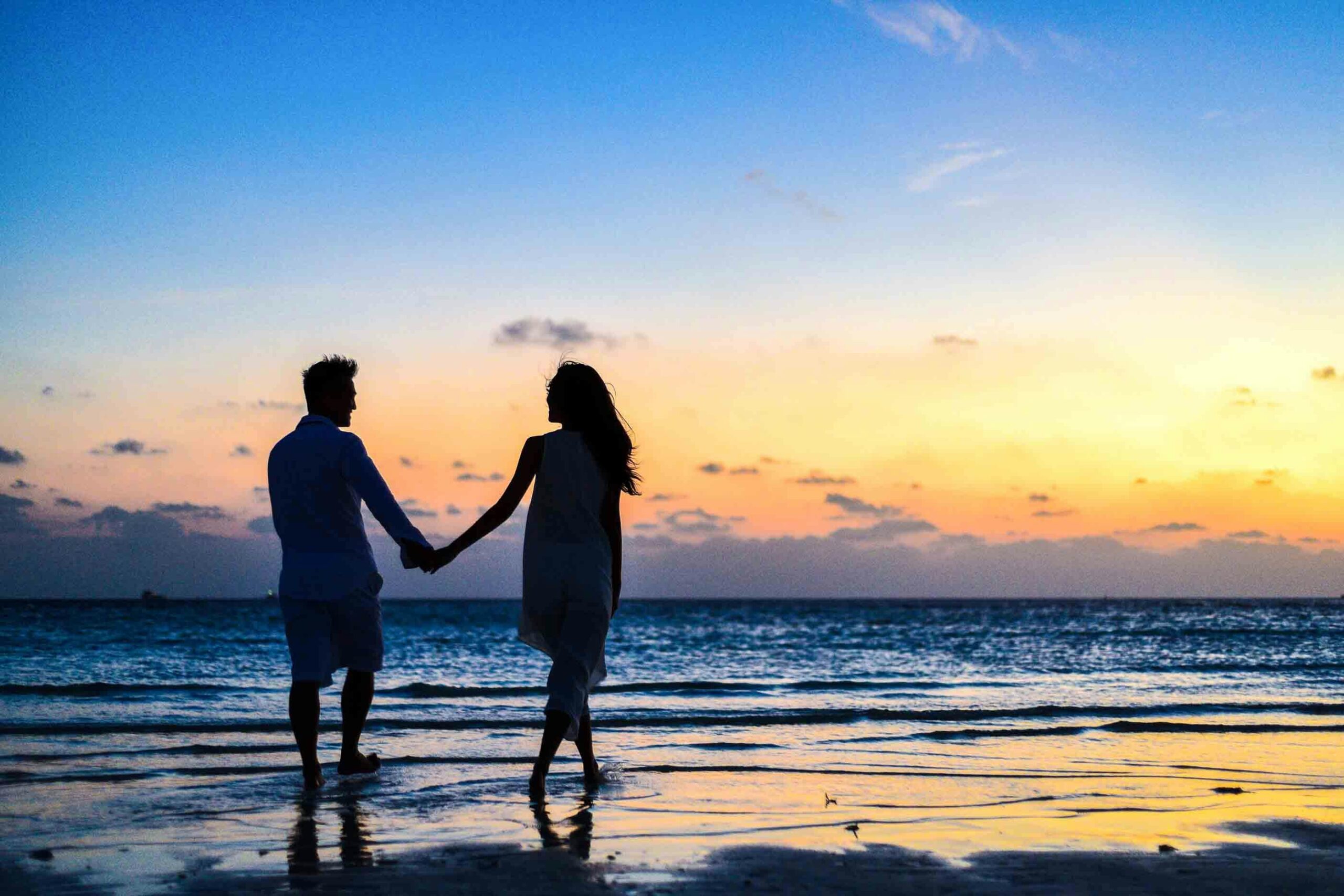 pexels-photo-1024960-1024960 A romantic couple walks hand in hand on a tropical beach at sunset, enjoying a serene moment together.