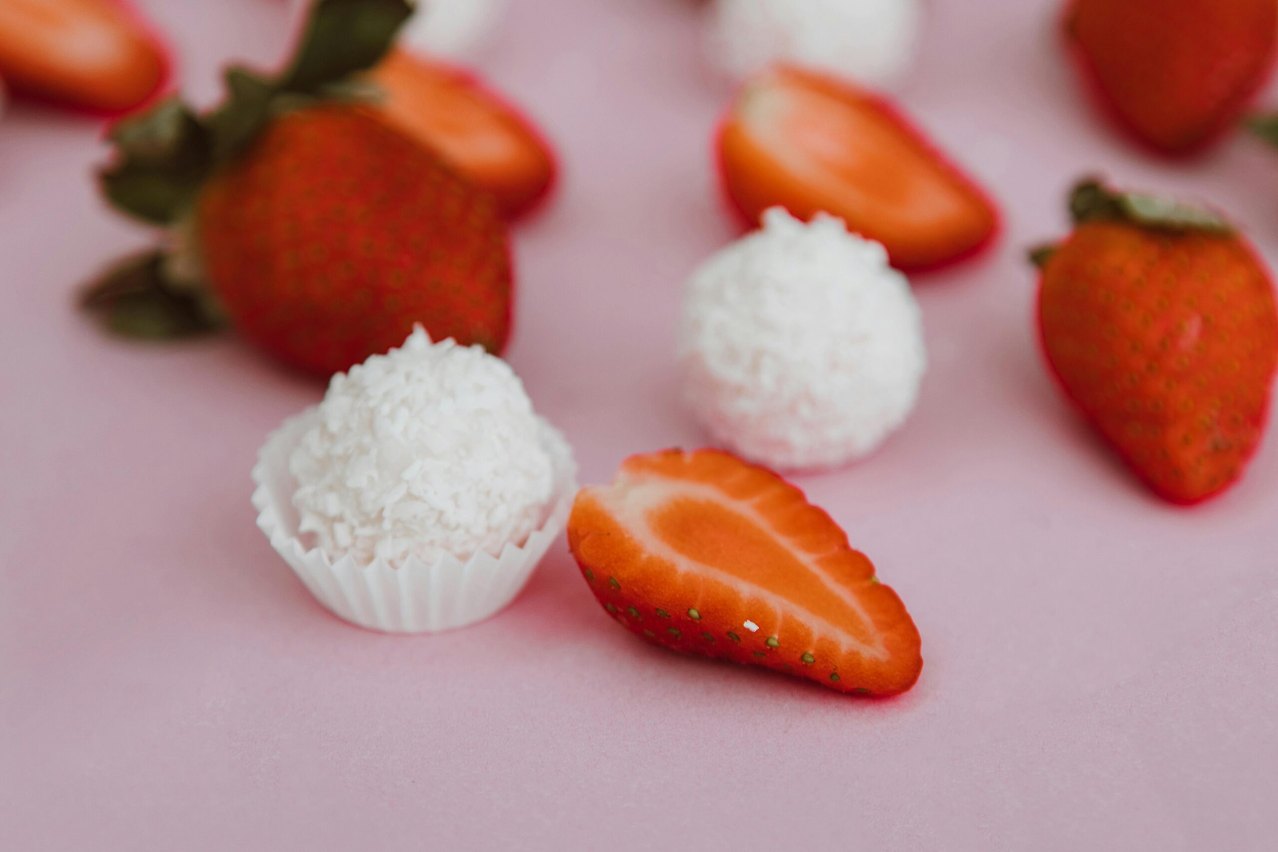 Delicious strawberries and coconut truffles on a pink background, perfect for dessert inspiration.
