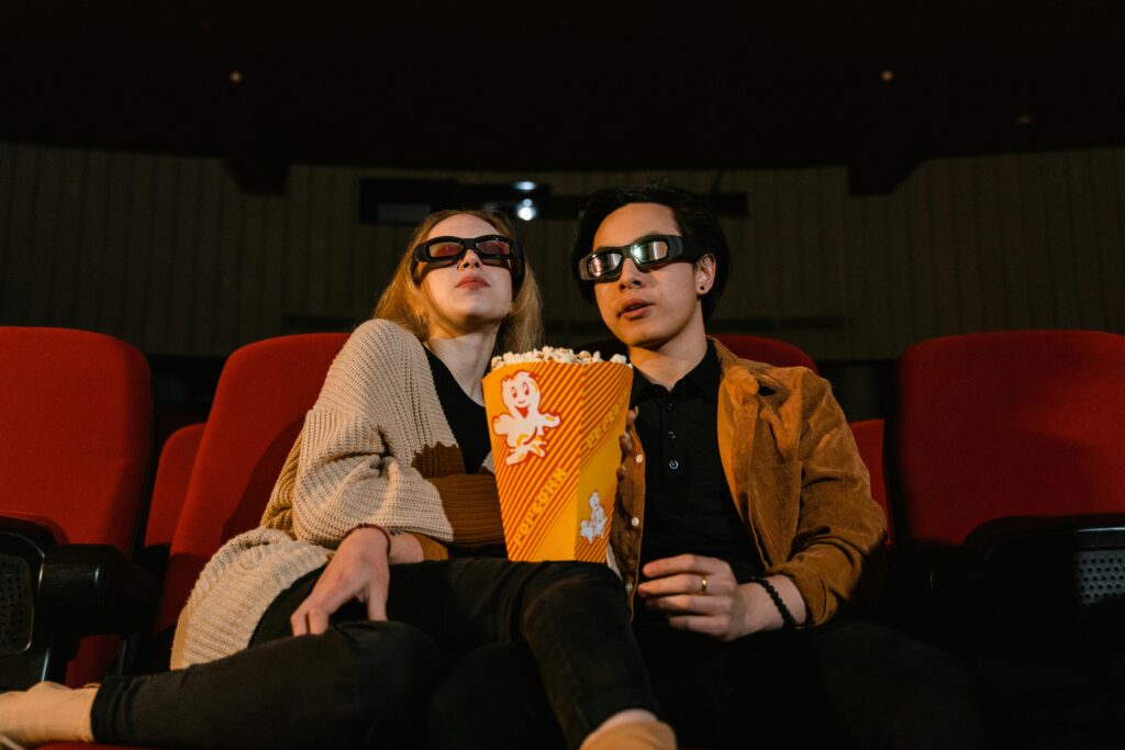 pexels-photo-7991144-7991144 Two adults wearing 3D glasses watching a movie with popcorn in a cinema setting.