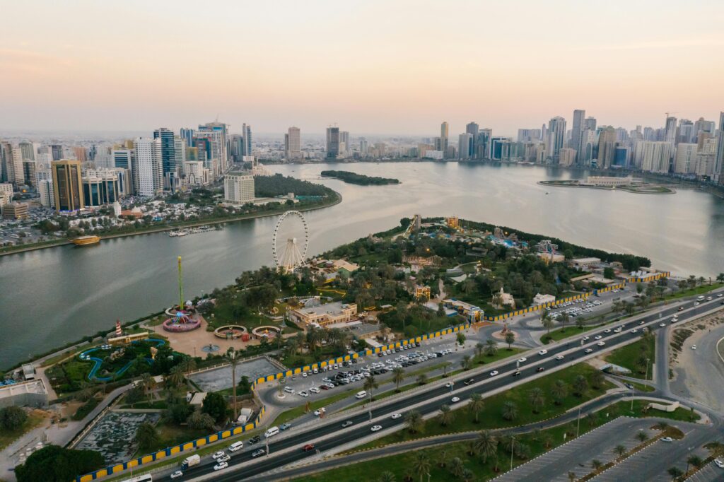 pexels-photo-8319477-8319477 A stunning aerial shot of Sharjah cityscape featuring parks, landmarks, and coastline at sunset.