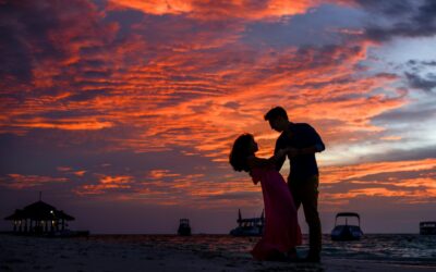 Silhouetted couple sharing a romantic moment on the beach during a stunning sunset.