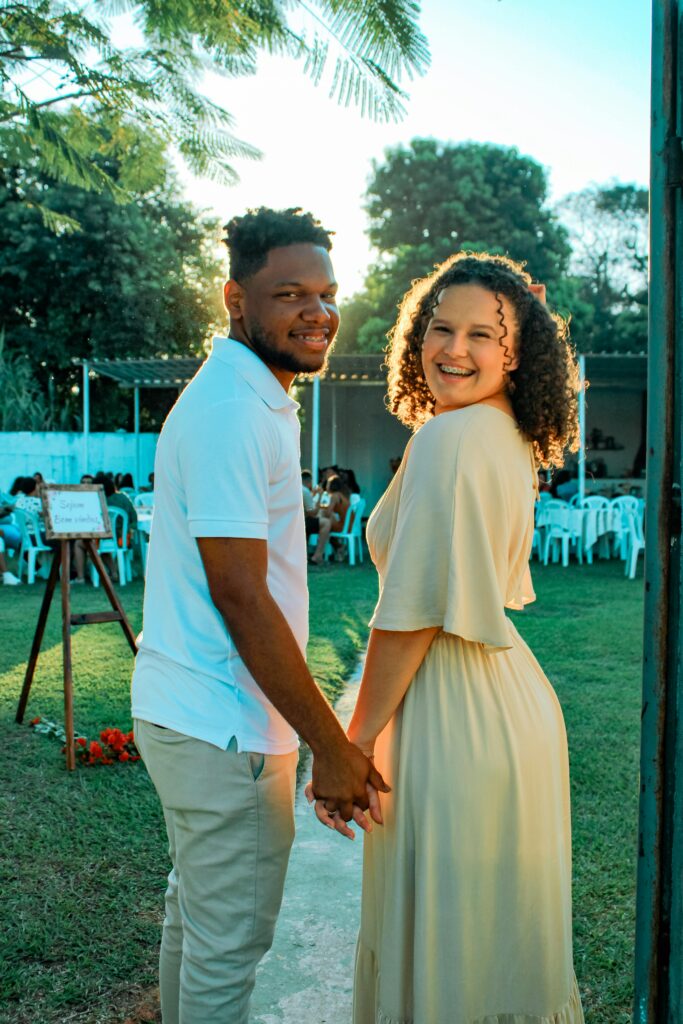 Smiling couple holding hands outdoors, exuding happiness at a sunny garden event.