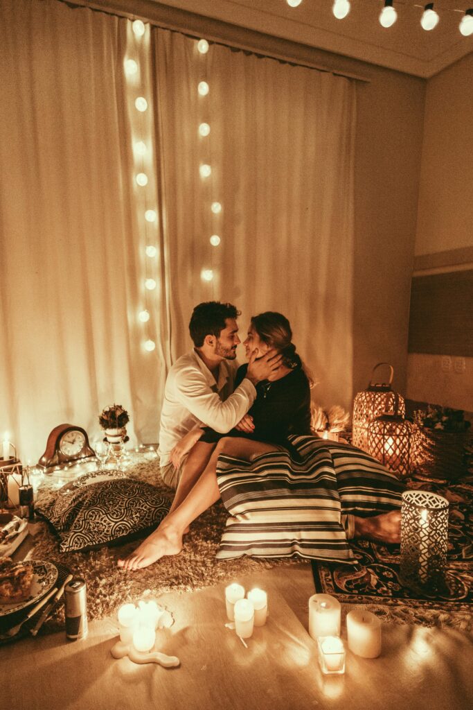 Couple embracing in a romantic candlelit room adorned with string lights.