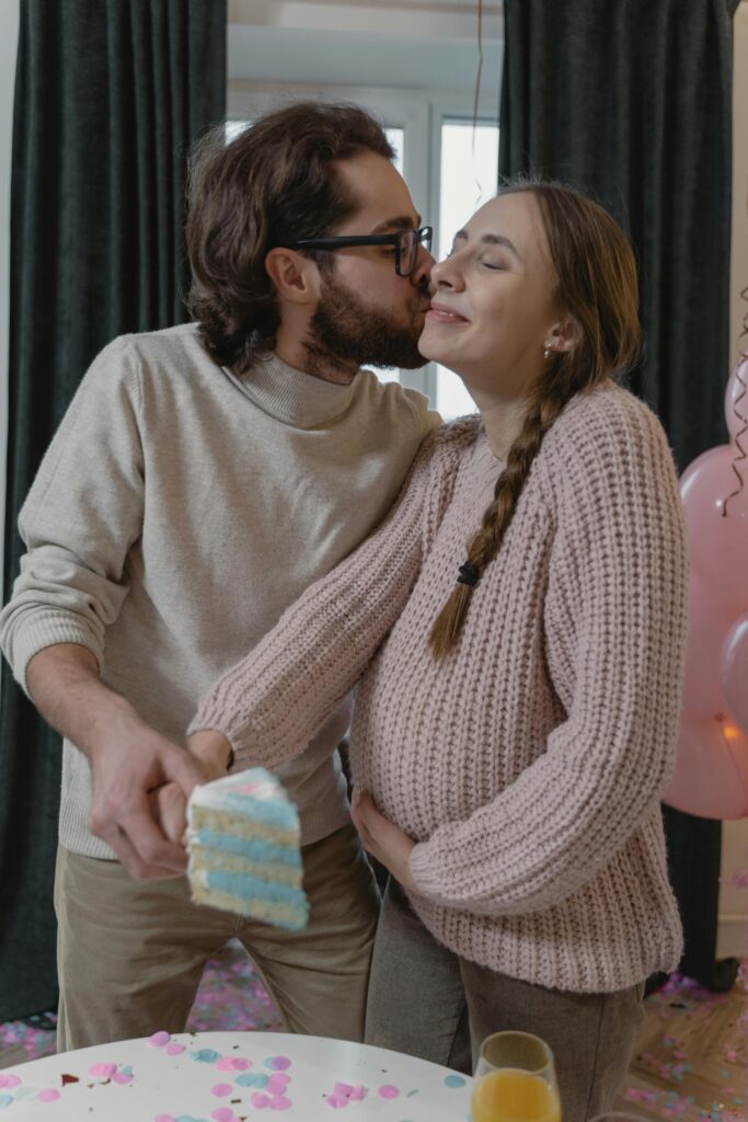 Happy couple celebrates gender reveal with cake and affection indoors.